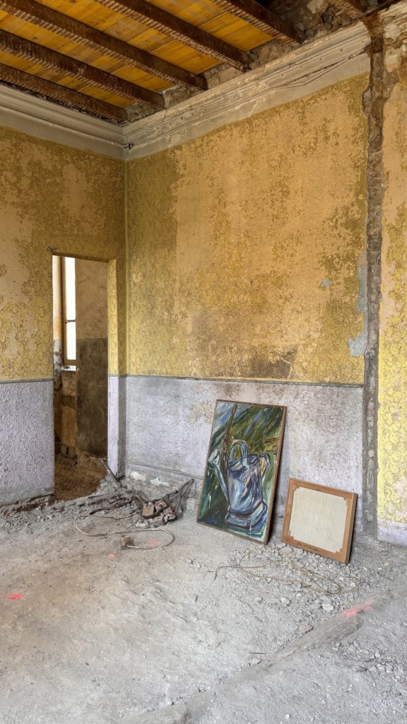 Mendrisio. Plinthe haute sous mur jaune, avec 2 tableaux posés au sol.